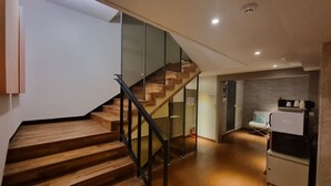 A modern interior with a wooden staircase, glass railings, and a kitchen area with a coffee machine. - Hound Hotel Seomyeon - Bumcheon (Busan)