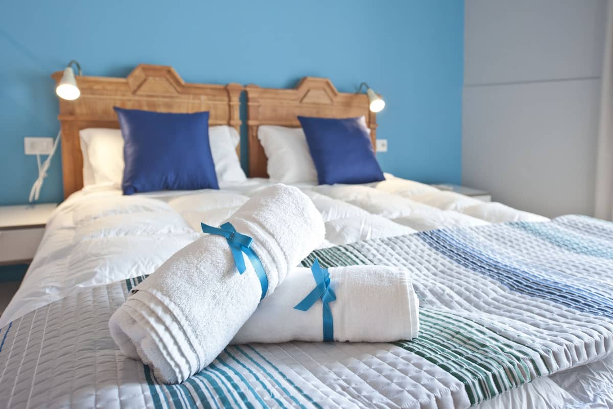 Una cama bien tendida con ropa de cama blanca y azul, dos almohadas azules y un cabecero de madera.