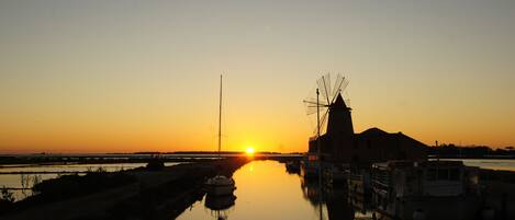 A sunset over a calm river with a windmill and boats.