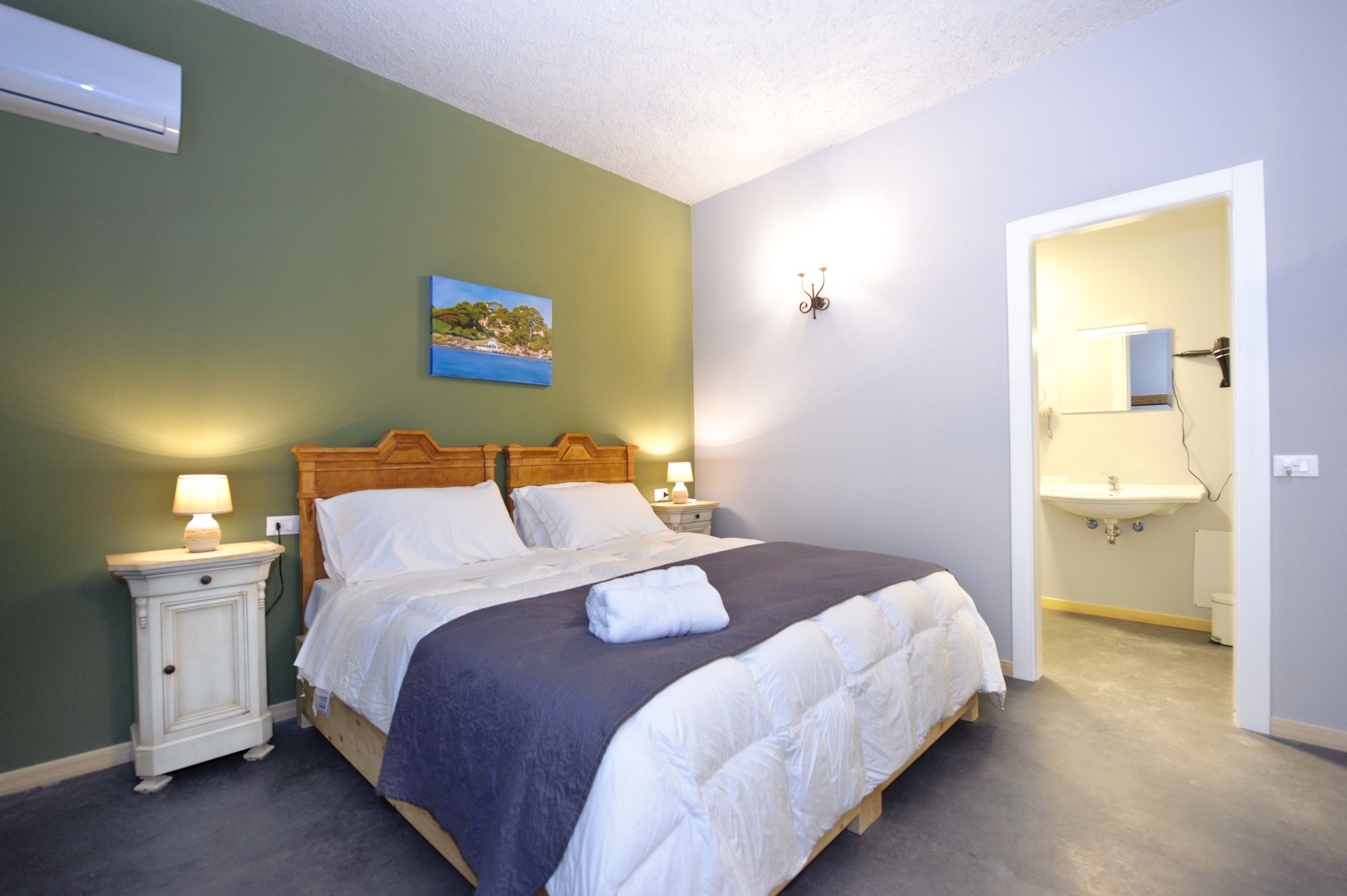 A neatly made bed with white linens, a nightstand with a lamp, and a painting on the wall.