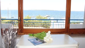 Un balcón con vista al mar, una mesa blanca con una revista y un ramo de flores.