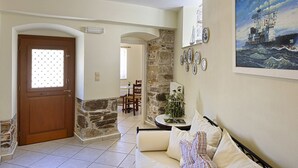 Un saló amb un sofà, una porta, una paret de pedra, un quadre i una zona menjador.