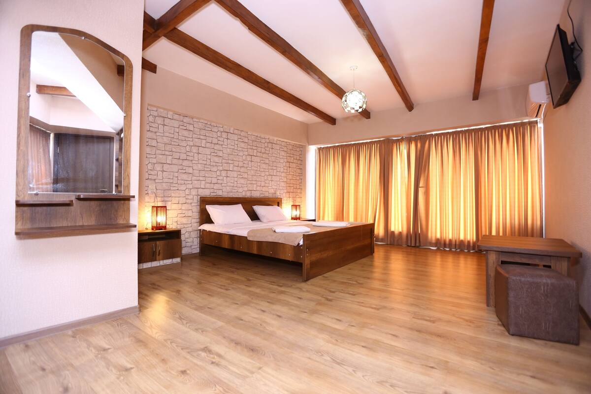 Un dormitorio con cama de madera, pared de piedra, vigas de madera y un amplio ventanal con cortinas.