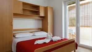 Habitación de hotel con cama, armario de madera y puerta corrediza de vidrio al exterior.