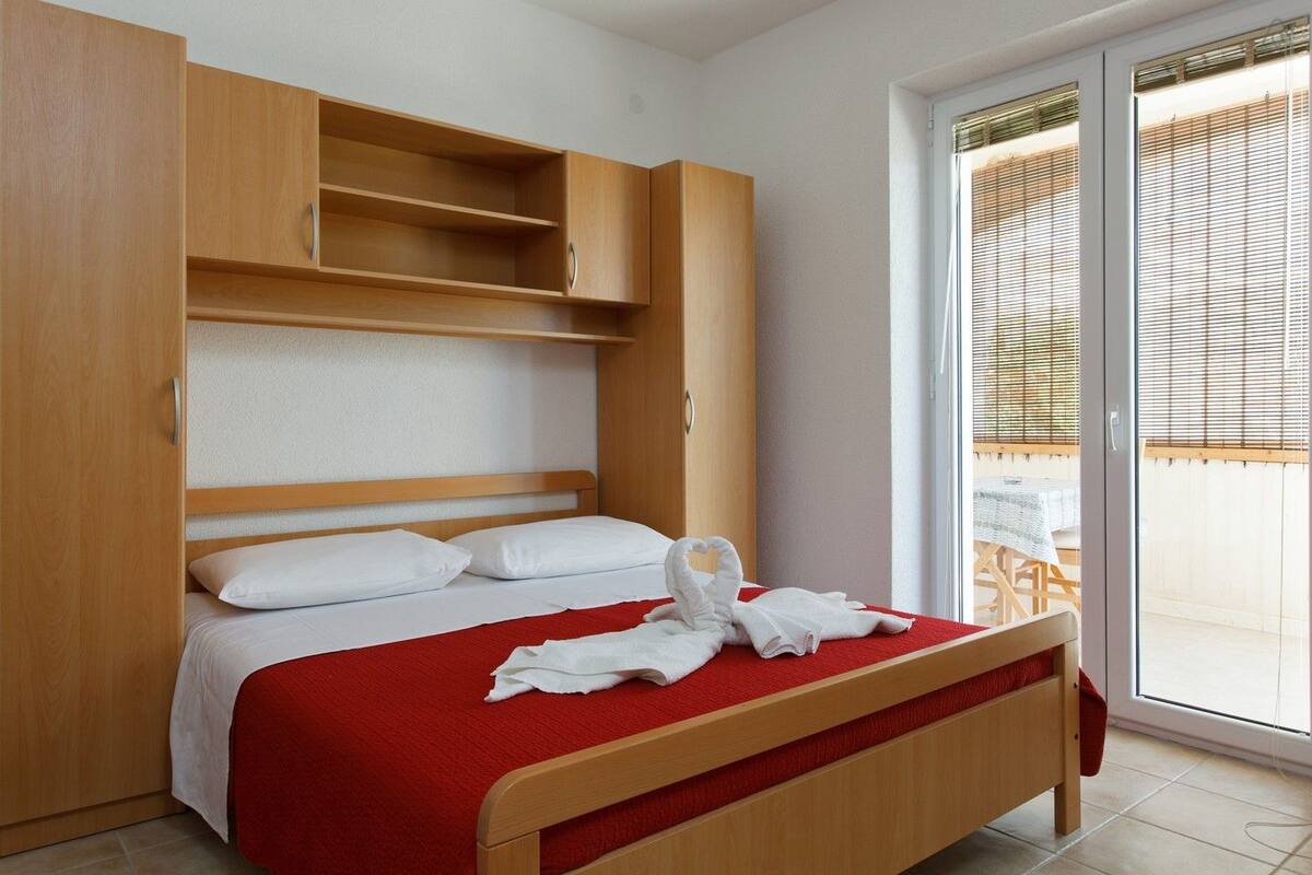 Habitación de hotel con cama, armario de madera y puerta corrediza de vidrio al exterior.