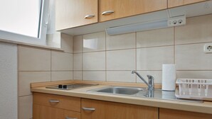 Una cocina con gabinetes de madera, un lavamanos de acero inoxidable, una estufa integrada y un ventanal sobre el lavamanos.