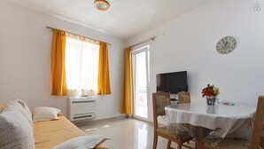 Habitación de hotel con cama, televisión, mesa de comedor con sillas, ventana con cortinas y un reloj en la pared.
