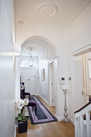 A hallway with white walls, an arched ceiling, and a dark rug leading to a door.