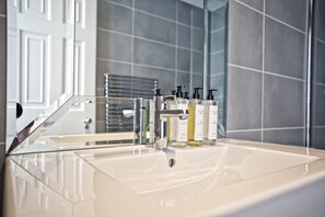 A bathroom with a white sink, chrome faucet, and toiletries.