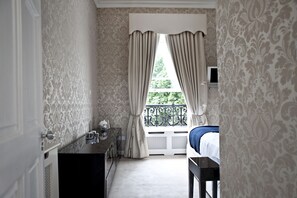 A hotel room with a bed, a desk, and a window with curtains.