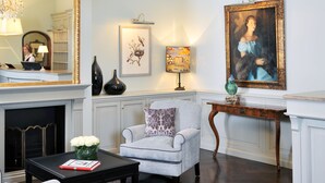 A living room with a fireplace, a white armchair, a coffee table, and a painting on the wall. - Hotel Kärntnerhof (Vienna)