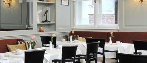 Un restaurante con varias mesas y sillas, manteles blancos y vistas al exterior a través de amplios ventanales.
