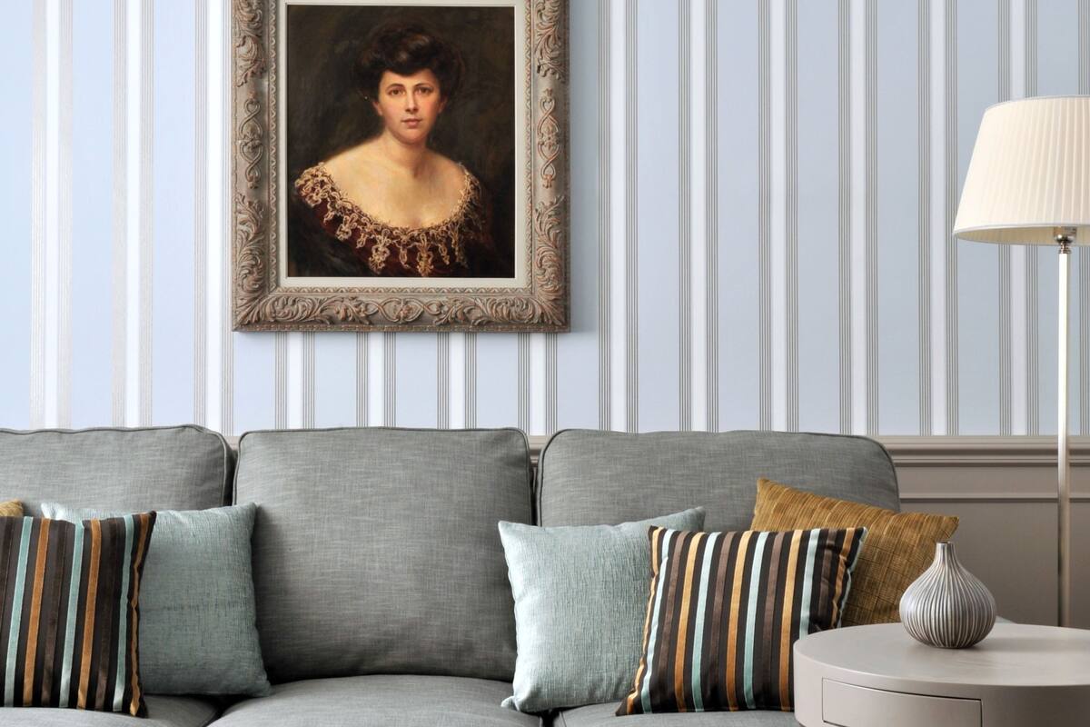 A grey sofa with striped cushions, a framed portrait on the wall, and a lamp on a side table.
