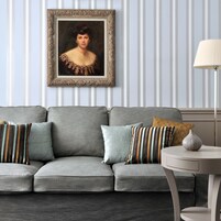 Um sofá cinzento com almofadas listradas, um retrato emoldurado na parede e uma luminária sobre uma mesa lateral.