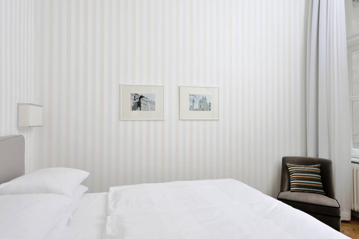 A hotel room with a bed, a chair, and two framed pictures on the wall.