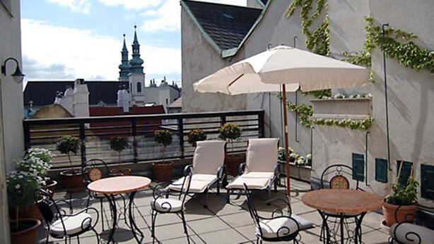 An outdoor patio with tables and chairs, potted plants, and a view of a building with a spire. - Hotel Kärntnerhof (Vienna)