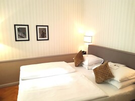 Una camera d'albergo con due letti, un comodino e due quadri appesi al muro.