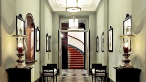A hallway with patterned flooring, a staircase, and wall-mounted sconces. - Hotel Kärntnerhof (Vienna)