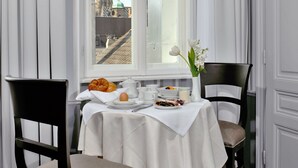 A dining area with a table set for breakfast, a window with a view of a cathedral, and a vase with flowers. - Hotel Kärntnerhof (Vienna)