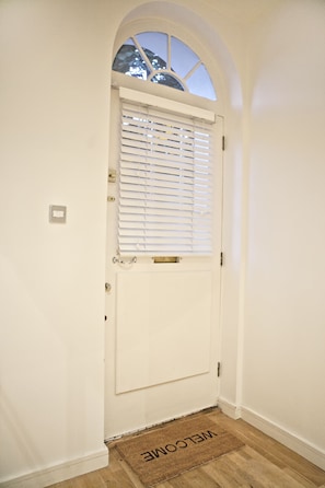 A white door with a window above it, a doormat with "WELCOME" written on it, and a light switch on the wall. - John Lennon Suite - hiphipstay (Dublin)