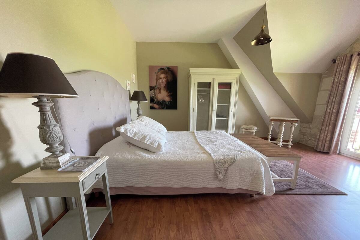 Ein Schlafzimmer mit Bett, Nachttisch, Lampe, Kleiderschrank und einem Fenster mit Vorhängen.