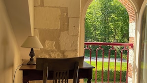 A room with a wooden table and chair, a lamp, and a view through an arched window to a garden.
