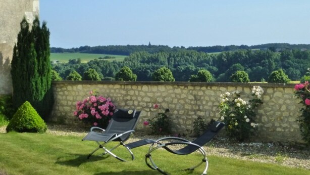 A stone wall with a garden and two reclining chairs facing a scenic view.