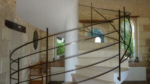 A spiral staircase with metal railings, a stone wall, and a view of greenery outside.