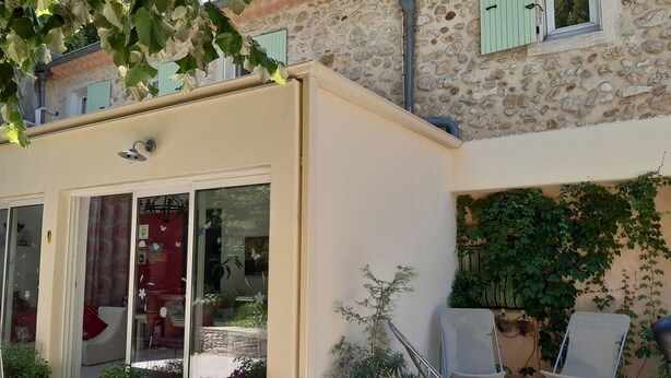 A cozy outdoor seating area with a stone building, potted plants, and a glass door entrance. - Louminai (Donzere)