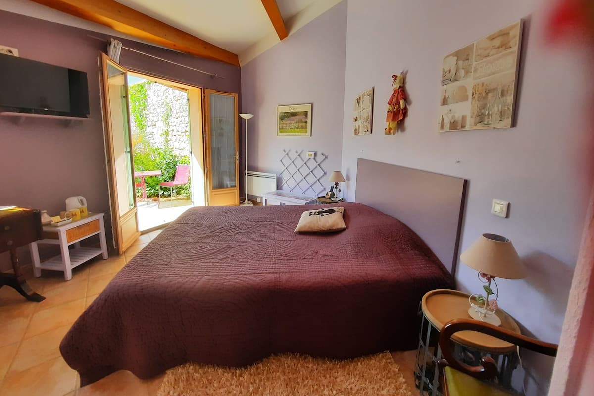 A bedroom with a large bed, a small table, a chair, a lamp, and a TV.