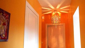 A hallway with an orange wall, a white door, and a globe-shaped light fixture. - Louminai (Donzere)