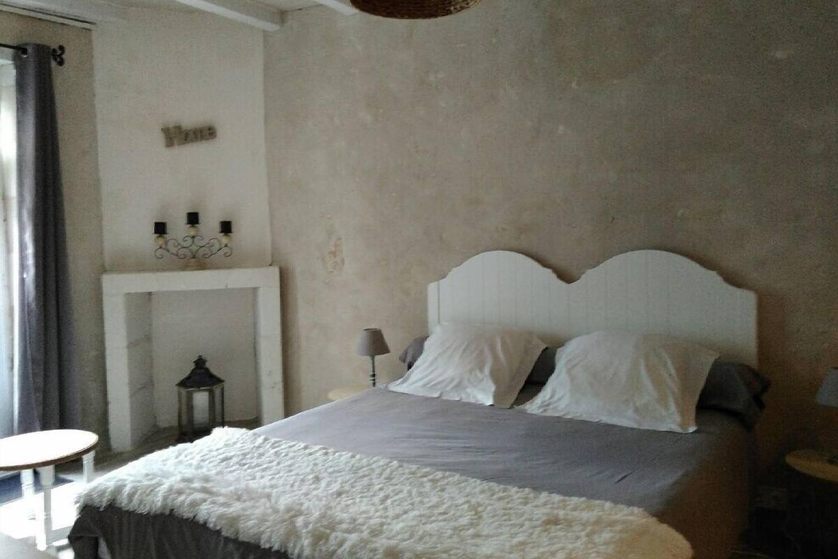 Ein Schlafzimmer mit Bett, einem kleinen Tisch, einer Lampe, einem Wandregal mit Dekoration und einer Pendelleuchte.