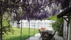 Une terrasse avec une table et des chaises, entourée d’un sol en briques et d’une végétation luxuriante.