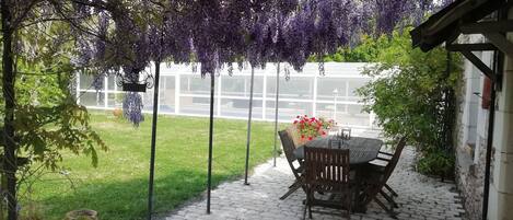 Un patio con una mesa y sillas, rodeado de piso de ladrillo y abundante vegetación.