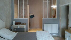 Une chambre à coucher comprenant un lit, une commode, un bureau, un panier suspendu, un miroir et un radiateur.