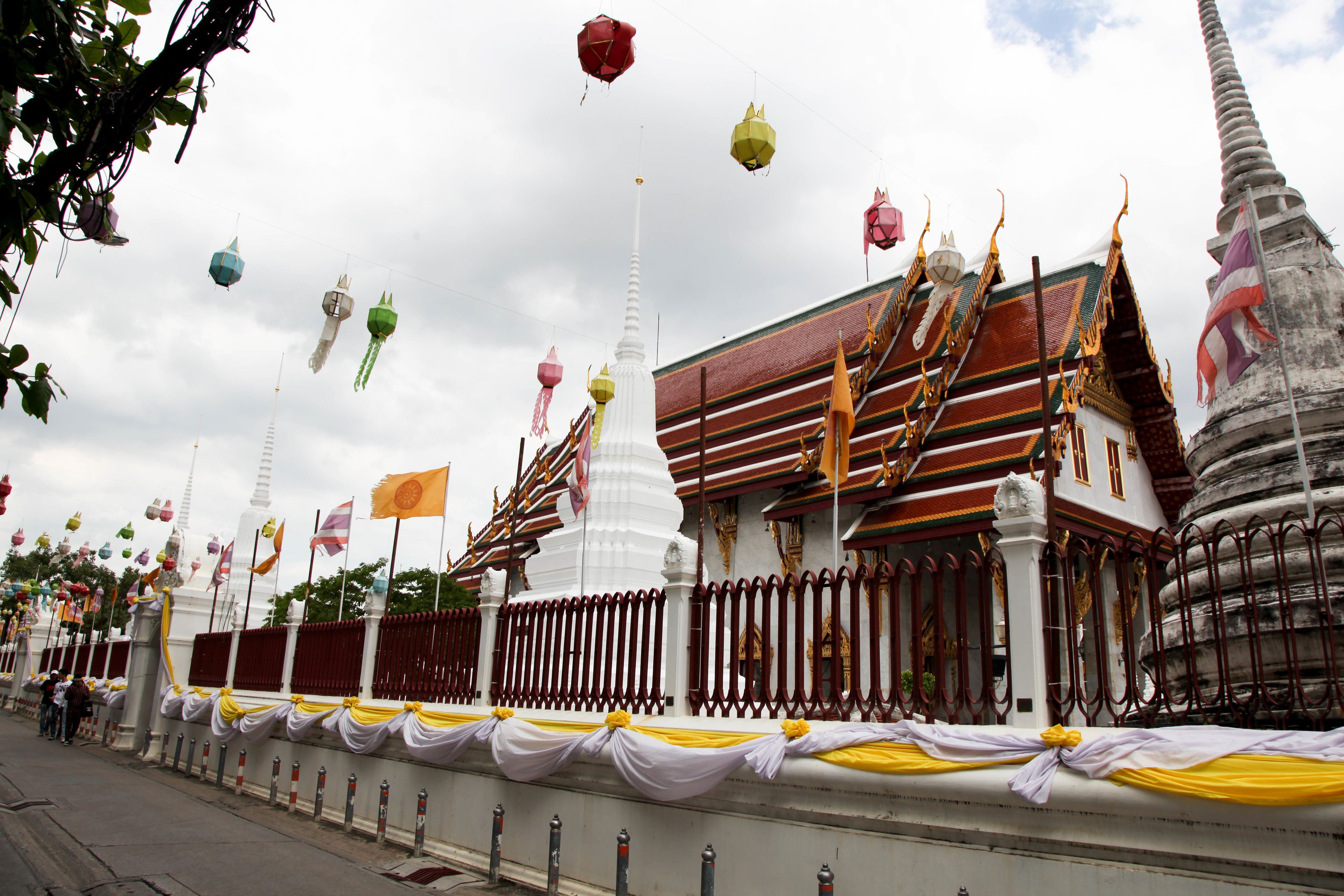 A traditional temple with multiple spires and a large central stupa, surrounded by a fence and draped with white and yellow fabric.