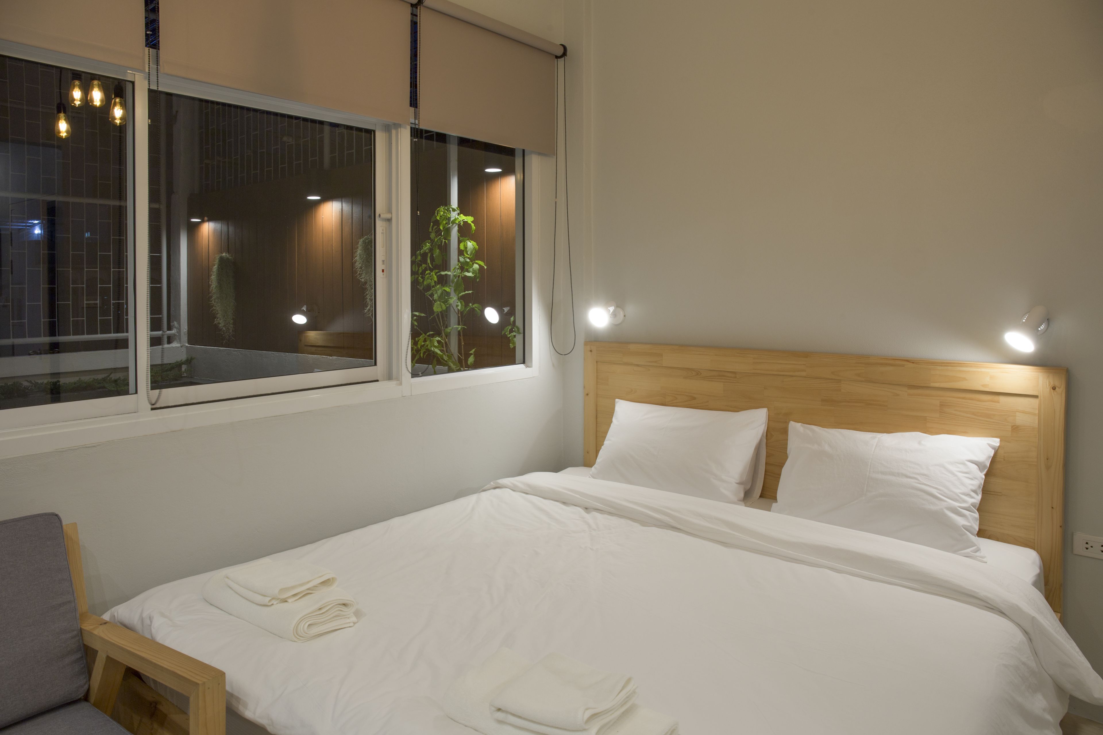 Uma cama bem arrumada com lençóis e almofadas brancos, uma cabeceira de madeira e uma janela com persianas.