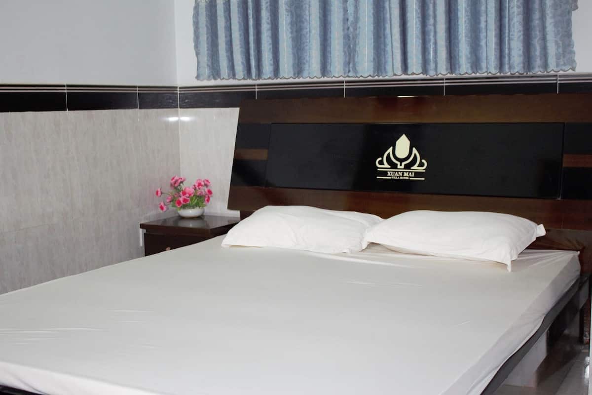 Ein Hotelzimmer mit Bett, Nachttisch mit Blumenvase und einer Kopfteil mit einem Logo.