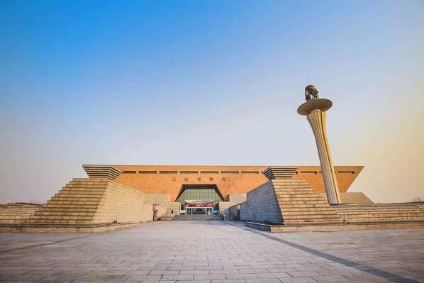 A large, open plaza with a prominent, tall, slender monument in the center.