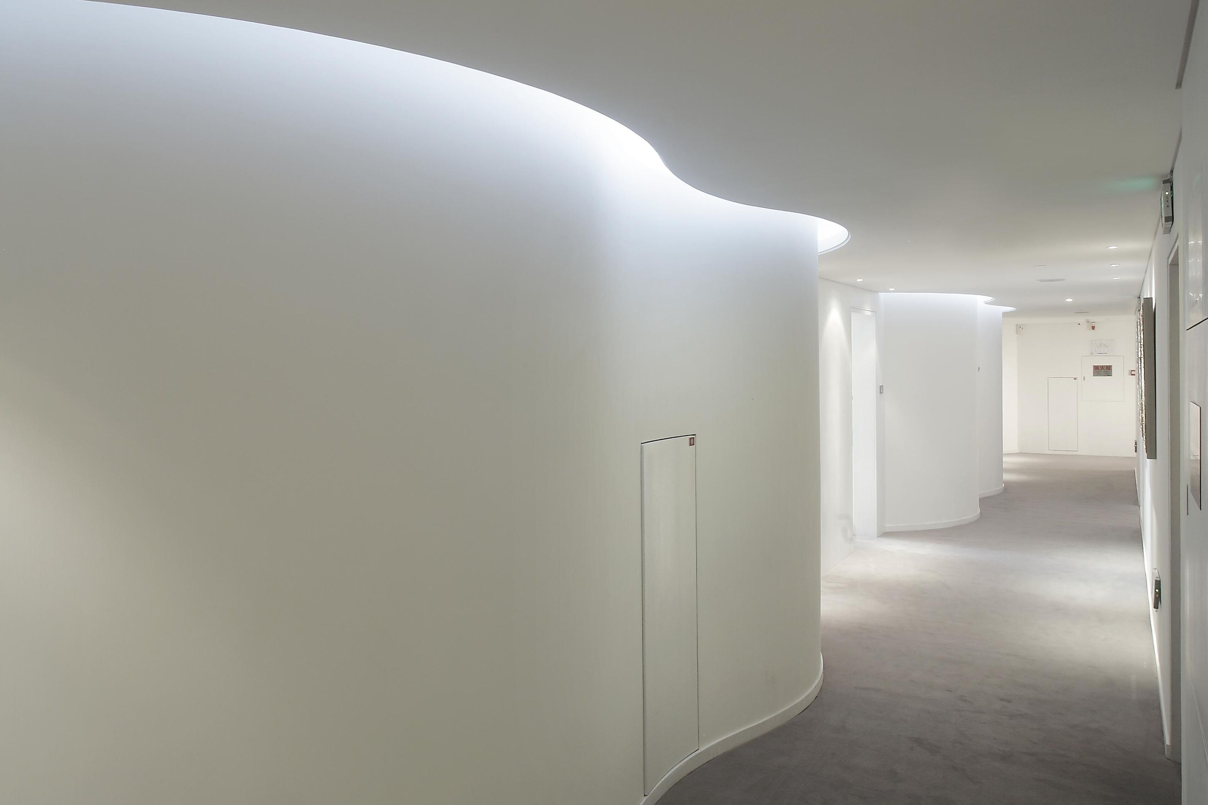 A modern, minimalist hallway with curved walls and recessed lighting.