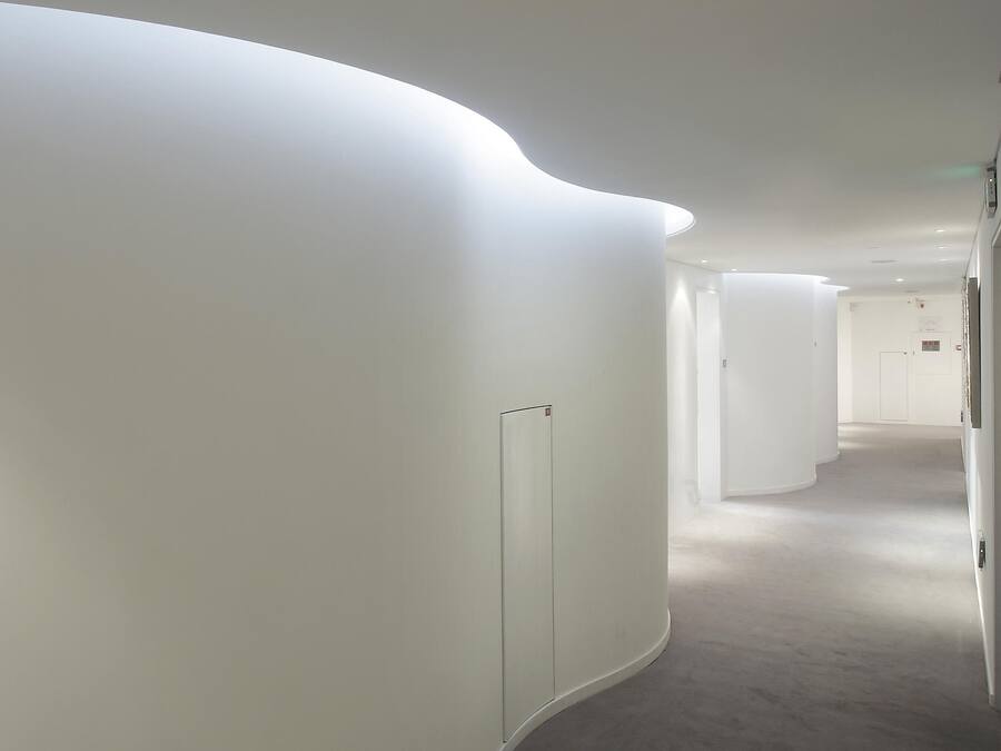 A modern, minimalist hallway with curved walls and recessed lighting.