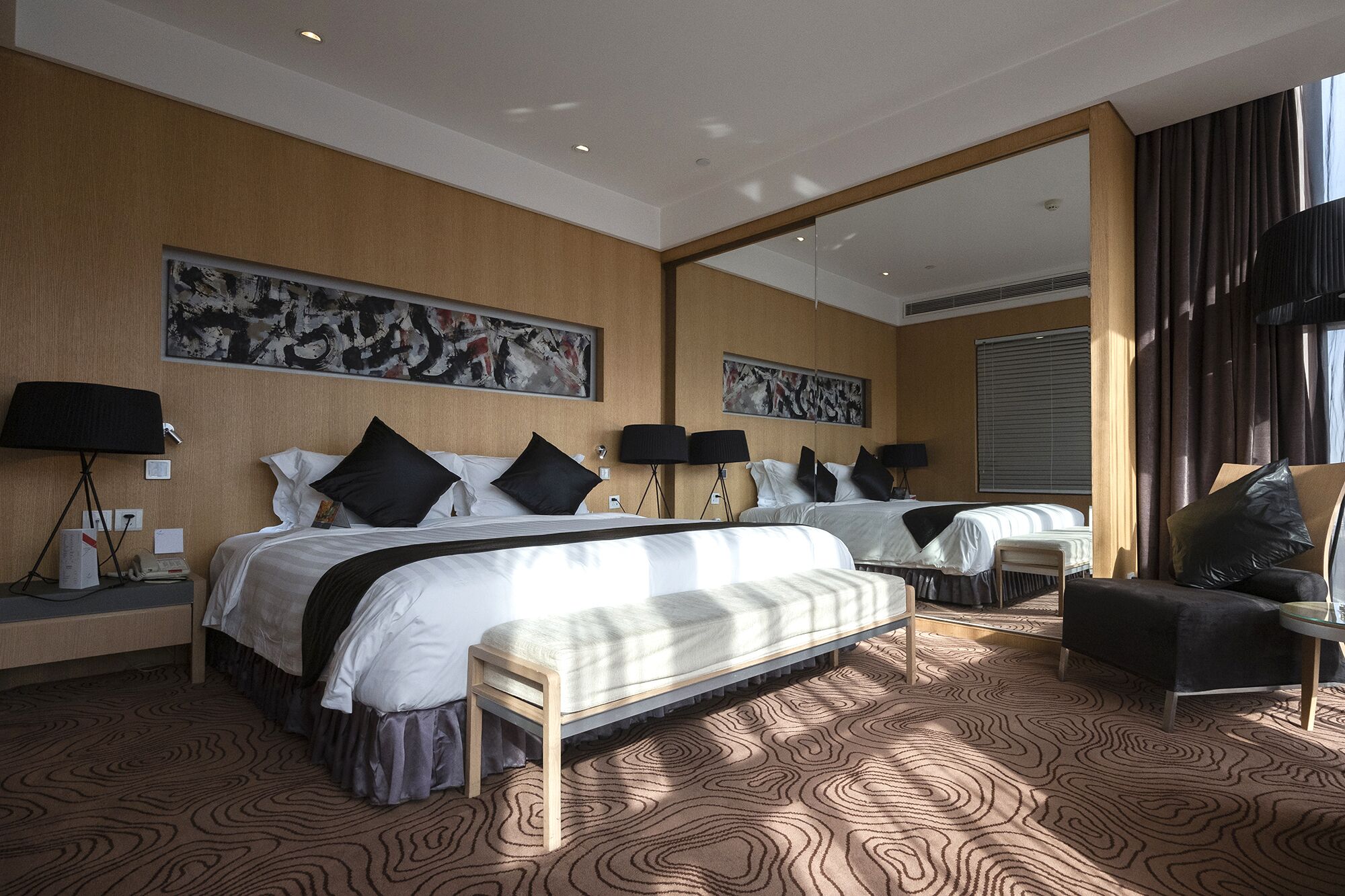A modern hotel room with two beds, a large mirror, and a seating area.