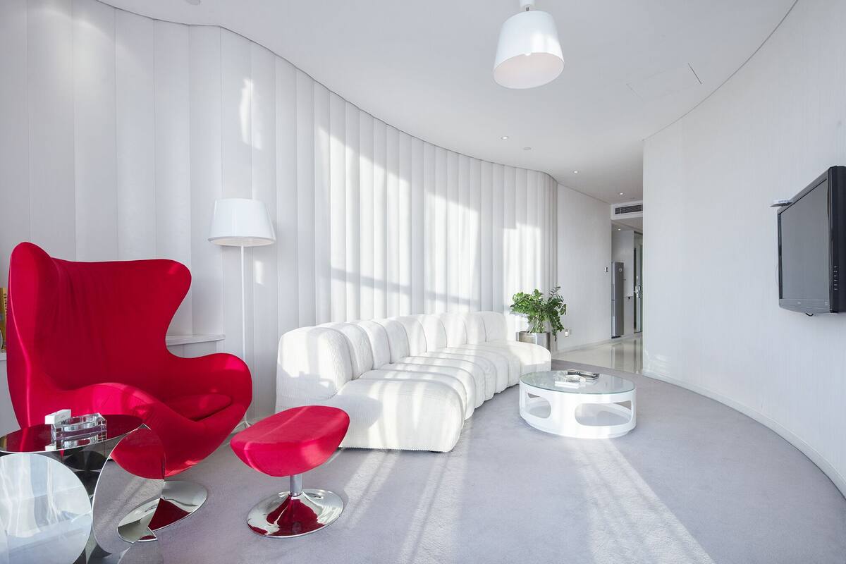 A modern living room with a white sofa, a red armchair, and a glass coffee table.