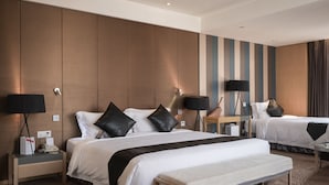 Quarto de hotel com duas camas, um banco, mesas de cabeceira, abajures e uma parede com listras verticais.