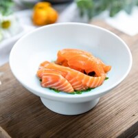 A white bowl containing slices of salmon on a wooden surface.