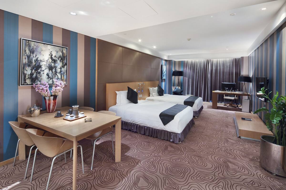 A hotel room with a large bed, a desk with a chair, a TV, and a coffee machine.