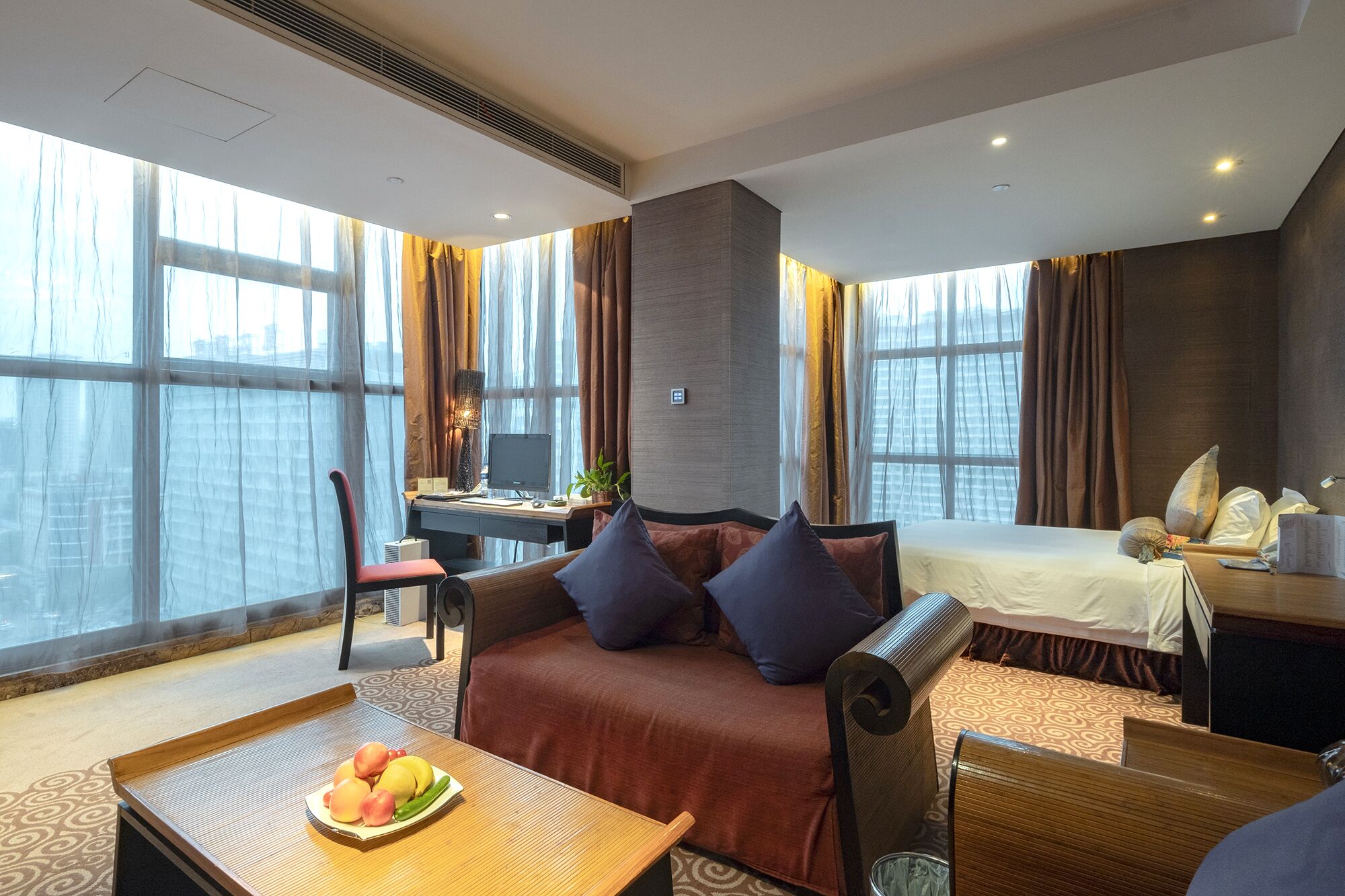 A hotel room with a sofa, a desk, a bed, and a view of the city.