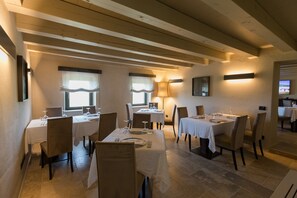 Un comedor con varias mesas dispuestas para comidas, con un techo de madera rústica y luz natural que entra por las ventanas.