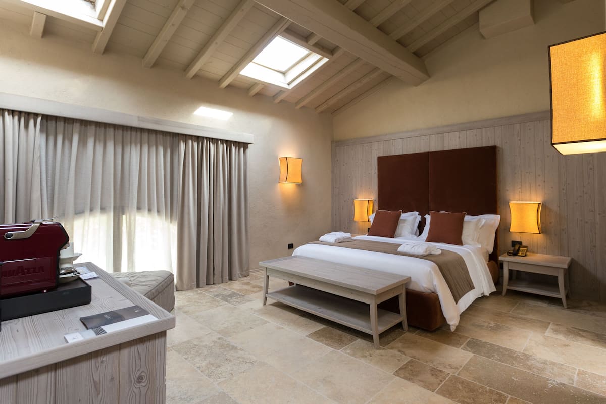 Une chambre d’hôtel avec un lit, des tables de chevet, un bureau avec un appareil rouge et une lucarne.