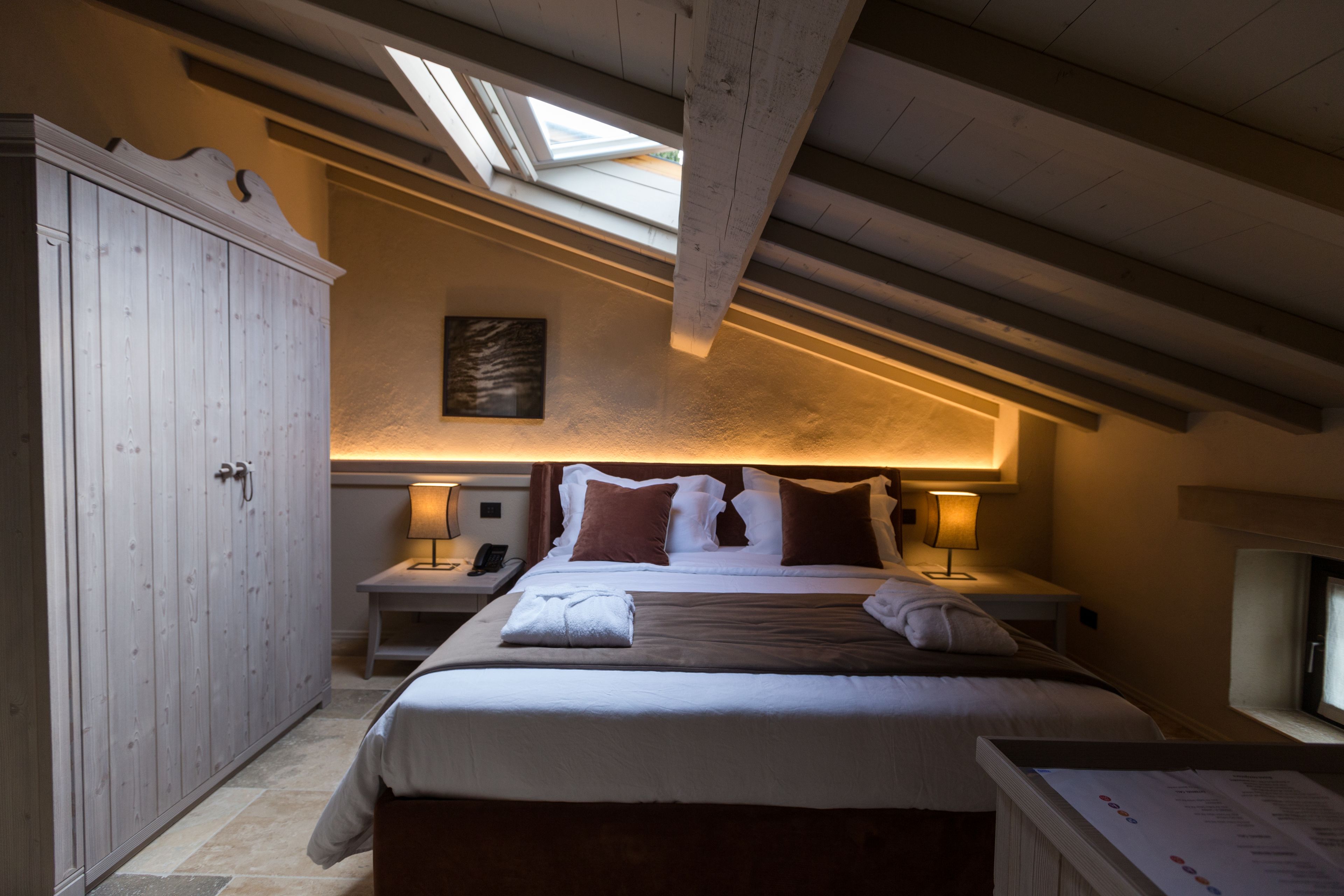 Une chambre avec un puits de lumière, un lit avec des oreillers, une table de chevet et une armoire.